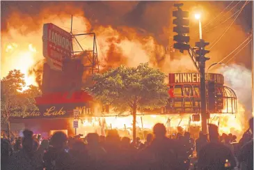  ?? PHOTOS BY AFP ?? Protesters gather in front of a liquor store in flames in Minneapoli­s, Minnesota.