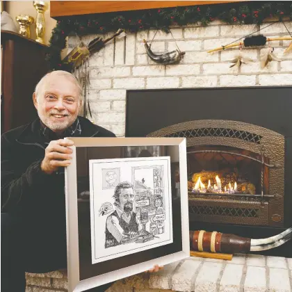  ?? ALLEN MCINNIS ?? Mike Reid holds an Aislin cartoon of his father, CJAD legend Paul Reid, as he sits by the fire on Wednesday. Reid said his father's beloved Christmas show is particular­ly appealing to Montrealer­s during the pandemic. Paul Reid died in 1983 at the age of 56, but his Christmas show lives on.