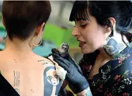  ??  ?? Tecniche
Nella foto in alto il tatuatore romano Snt, 33 anni, mentre esegue un lavoro sul volto di Achille Lauro; sotto una tatuatrice all’opera in uno stand della kermesse