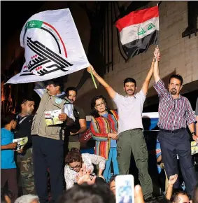  ?? AP/KARIM KADIM ?? Iraqis celebrate while holding national flags in Tahrir square Monday in Baghdad.