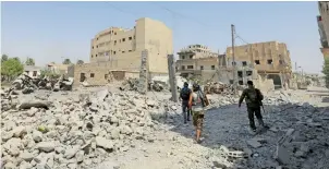  ??  ?? Fighters from the Syrian Democratic Forces walk through rubble in the embattled city of Raqqa.