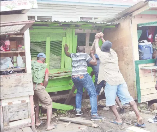  ?? (Orlando Charles photo) ?? Labourers using a length of wood to ease a stall off the road before pushing it onto the pavement behind.