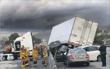  ?? Gina Ferazzi Los Angeles Times ?? RESCUE PERSONNEL work on the 60 Freeway in East Los Angeles after a big rig went through the center divider, crushing a car and causing several other vehicles to crash on the rain-slicked lanes on Jan. 5.