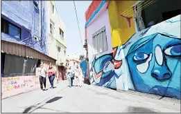  ??  ?? People walk past houses, painted as part of the ‘Ouzville’ project, in Beirut’s southern Ouzai neighborho­od, on Aug 19, 2017 (AFP)