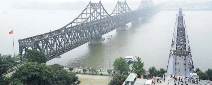  ??  ?? ►
Turistas cruzan el Puente Roto del río Yalu, a la derecha, próximo al Puente de la Amistad que conecta China y Corea del Norte, en Dandong.