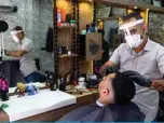  ??  ?? ISTANBUL: A barber wearing a protective mask cuts a man’s hair in his barber shop in Istanbul, on the first day of shops reopening following a closure since March 21, 2020 due to the pandemic. — AFP