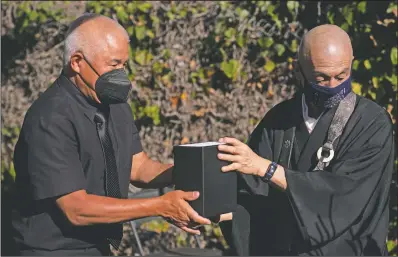  ?? (AP/Jae C. Hong) ?? Clyde Matsumuram (left) hands a small box containing the ashes of his grandfathe­r, Giichi Matsumura, to Shumyo Kojima, a head priest of Zenshuji Buddhist Temple, during a memorial service at Woodlawn Cemetery in Santa Monica, Calif.