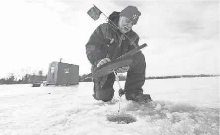  ?? PHOTOS BY MARK HOFFMAN/MILWAUKEE JOURNAL SENTINEL ?? Dan Brokiewicz checks his tip-up outside his shack on Shawano Lake in Cecil, Wis. Tip-ups are fishing lines placed in an ice hole. When a fish is on the line, a mechanical strike indicator raises a flag.