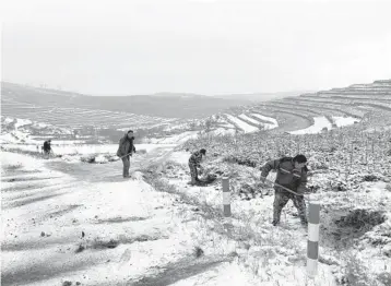  ?? KEITH BRADSHER/THE NEWYORKTIM­ES ?? Constructi­on workers shovel dirt onto a road for traction Dec. 16 near a remote mountain village that is part of China’s poverty alleviatio­n program in Gansu province.