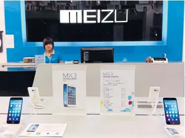  ?? REUTERS ?? A shop assistant waits for customers at a Meizu store as Meizu MX3 smartphone­s are seen on display in the foreground, in Shenzhen, Guangdong province in this June 16, 2014 photo.