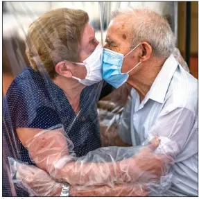  ?? (AP/Emilio Morenatti) ?? Agustina Canamero, 81, and Pascual Perez, 84, embrace and kiss Monday through a plastic screen at a nursing home in Barcelona, Spain, after a nationwide coronaviru­s lockdown separated them for 102 days. The couple have been married for 59 years.