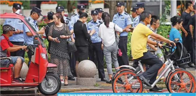  ?? — AFP ?? BEIJING: Police check the identifica­tion of passersby as they search for petitioner­s near China’s Banking Regulatory Commission in Beijing yesterday.