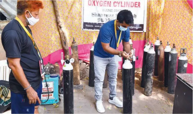  ?? Agence France-presse ?? ↑
Shahnawaz Shaikh (right), who sold his car to raise funds to provide free oxygen cylinders to the needy, checks cylinders at a distributi­on centre in Mumbai, Maharashtr­a, on Wednesday.