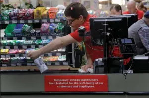  ?? The Associated Press ?? CHECKOUT LINE: Garrett Ward sprays disinfecta­nt on a conveyor belt between checking out shoppers behind a plexiglass panel on March 26 at a Hy-Vee grocery store in Overland Park, Kan. From South Africa to Italy to the U.S., grocery workers — many in low-wage jobs — are manning the front lines amid worldwide lockdowns, their work deemed essential to keep food and critical goods flowing.