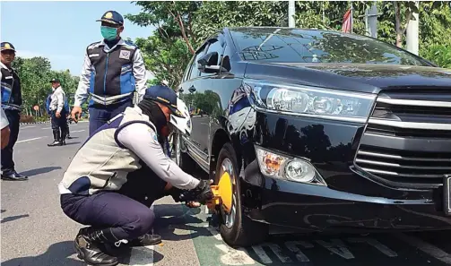  ?? THORIQ/JAWA POS ?? TAK PANDANG BULU: Ban mobil yang diparkir di tepi frontage barat terpaksa digembok petugas karena parkir sembaranga­n dan ditinggal pemiliknya.