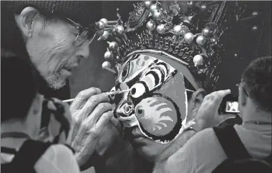  ?? FENG JIE / XINHUA ?? A visitor at an exhibition at the Shandong Art Museum in Jinan, Shandong province, on Wednesday takes a picture of one of the photograph­s on display — an elderly man painting a traditiona­l headpiece. About 200 photos featuring the country’s intangible...