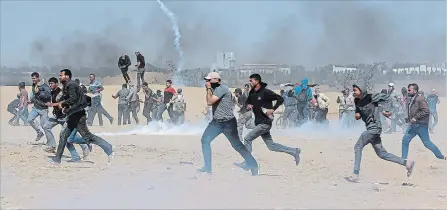  ?? ADEL HANA THE ASSOCIATED PRESS ?? Palestinia­n protesters run for cover from teargas fired by Israeli troops near the border fence, east of Khan Younis, in the Gaza Strip, Tuesday.