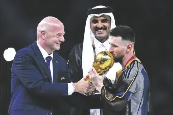  ?? AP PHOTO/MANU FERNANDEZ ?? Argentina’s Lionel Messi kisses the trophy presented by FIFA President Gianni Infantino (left) as The Emir of Qatar Sheikh Tamim bin Hamad Al Thani looks on, after the World Cup final soccer match between Argentina and France at the Lusail Stadium in Lusail, Qatar, on Dec. 18, 2022.