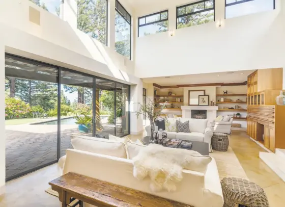  ?? Vanguard Properties ?? A soaring ceiling crowns a living room at 110 Idlewood Road in Kentfield with concrete flooring and access to a pool patio. Built-in shelving, speakers and a wood-burning fireplace accent the space.