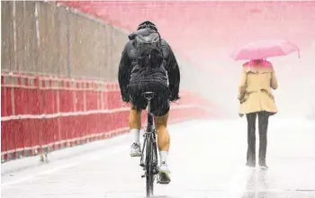  ?? MARY ALTAFFER AP ?? A pedestrian and cyclist make their way over a bridge in a heavy downpour Tuesday in New York. The storm that brought flash flooding to New York took out power to nearly a half-million homes in New England.