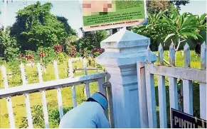 ??  ?? No entry: A man is seen locking Pulau Melaka Muslim cemetery gates.
