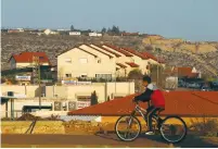  ?? (Baz Ratner/Reuters) ?? A BOY RIDES his bicycle past houses in the Ofra settlement on February 6.