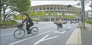  ?? (AP/Eugene Hoshiko) ?? People wearing protective masks s ride bicycles near the Japan National Stadium, where opening ceremony and many other events are planned for the Olympics in Tokyo.