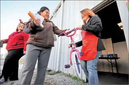  ?? Staff Photo by Tim Barber ?? Isabel Lopez Mendez, center, is presented a bicycle for her daughter by volunteer Francine Benzmiller, right, Tuesday at the Salvation Army warehouse in Rossville. Kimberly George watches the exchange, at left.