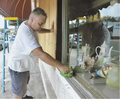  ?? PHOTOS BY PATTI BLAKE/NEWS HERALD VIA AP ?? GETTING PREPARED: Bobby Smith boards up the windows at Jani’s Ceramics in Panama City, Fla., yesterday while Tallahasse­e Mayor Andrew Gillum, below left, helps Eboni Sipling fill up sandbags.