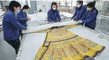  ?? PHOTOS BY ZOU HONG / CHINA DAILY ?? From top: A Palace Museum conservato­r restores a silk painting. Textile conservato­rs examine a royal robe.