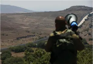  ?? (Ronen Zvulun/Reuters) ?? AN IDF SOLDIER speaks over a megaphone to Syrians standing near the border fence with Israel yesterday.