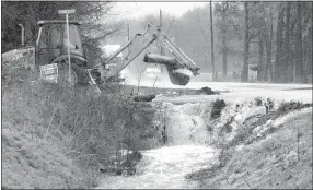  ?? Westside Eagle Observer/MIKE ECKELS ?? A Benton County road worker removes a large log that was wedged in a culvert as a torrent of water flows over the roadway at the intersecti­on of Arkansas Highway 12 and South Pleasant Valley Road near Springtown on March 27.