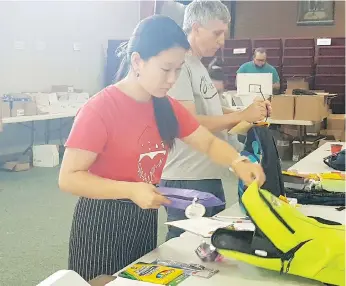  ?? ALEXA LAWLOR ?? Angela Luo and Randy Robertson help fill backpacks for the Salvation Army’s back-to-school backpack program on Tuesday. This year, the initiative will provide 1,000 backpacks to children in need.