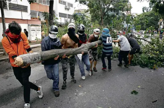  ?? Carlos Garcia Rawlins/Reuters ?? Manifestan­tes mascarados usam árvore para montar uma barricada na zona leste de Caracas; protestos violentos deixaram dois mortos na Venezuela