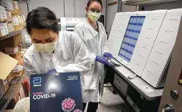  ?? Bob Owen / Staff file photo ?? Colory Bun, left, a molecular technology pathologis­t, displays ID Now, a virus screening that offers a diagnosis within minutes, at Methodist Hospital in April.