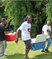  ??  ?? Messiah Cooper and community member James Tucker carry a water cooler as they set-up Friday afternoon in 10th Street Park for a community barbecue.