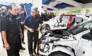 ??  ?? Holdings CEO Datuk Ahmad Fuaad Mohd Kenali (right) showing Comm Mazlan the inner workings of the car which was donated for use as a training tool to police mechanics.