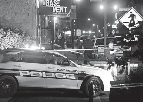  ?? AP/ JONESBORO SUN/ STACI VANDAGRIFF ?? An officer lifts crime scene tape Sunday morning to let a police cruiser through at the scene of a fatal shooting in downtown Jonesboro. One person was killed and six others were injured.