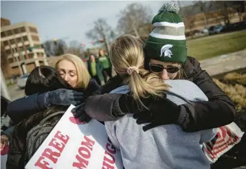  ?? JAKE MAY/THE FLINT JOURNAL ?? Spartan hug: Sue Dodde, a mother from Conklin, Michigan, right, embraces a student with a“free hug from a mom”as the campus reopened for classes Monday at Michigan State University in East Lansing, Mich. One week ago, three students were killed and five others were injured during a mass shooting at the university.