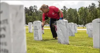  ?? AJC 2021 ?? Last year, Patsy Hurst placed an American flag near a headstone at the Georgia National Cemetery in Canton. Flag placement on headstones began Friday and will end today. The event was canceled last year due to COVID-19.