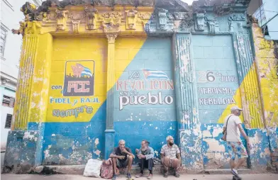  ?? RAMON ESPINOSA/AP 2020 ?? Cuba is implementi­ng deep financial reform in hopes of stemming an economic crisis and reconfigur­e a system that will still grant some universal benefits, including free health care. Above, people sit against a wall with political slogans in Havana.