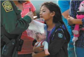  ?? JOHN MOORE GETTY IMAGES AGENCE FRANCE-PRESSE ?? La petite Stefany Marjorie, âgée de 8 ans, regarde un agent des douanes américaine­s vérifier les informatio­ns de sa famille à leur arrivée à Mission, au Texas.