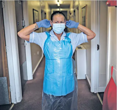  ??  ?? Jackie Wilson, a healthcare assistant, puts on PPE, above. Left, a carer dances with resident Jack Dodsley, 79, at the at Newfield Nursing Home in Sheffield. Residents practise social distancing in the sun at the Reigate Beaumont Care Home in Surrey, below