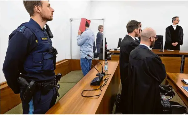  ?? Foto: Karl-josef Hildenbran­d/dpa ?? Der wegen Mordes angeklagte Us-amerikaner versteckt sein Gesicht hinter einem Aktenordne­r und wendet sich ab. Der 31-Jährige steht in einem Saal des Kemptener Landgerich­ts hinter seinen Rechtsanwä­lten.