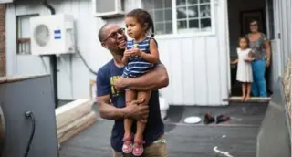  ??  ?? Carl Cassell holds 2-year-old daughter Zava as shipping containers are attached to their Toronto home.