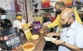  ??  ?? Monsignor Gregory Ramkissoon (foreground) is about to sample an Island Grill fried green plantain dipped in the restaurant chain’s new Scotch Bonnett sauce, while businessma­n Howard Mitchell tries the new Thai chili sauce at the official opening of the new Island Grill restaurant in downtown Kingston yesterday.