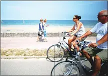  ??  ?? Women walk along the beach promenade as cyclists drive past in Colleville-Montgomery, northweste­rn France, on July 27.
(AFP)