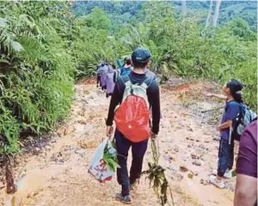  ??  ?? Schoolchil­dren trudging along the muddy path to reach SK Buayan.