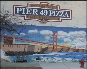  ??  ?? A mural depicting the Golden Gate Bridge now brightens up the side of the Pier 49 Pizza building in downtown Springvill­e. The mural was painted by local artist Mark Shipley, pictured at right.