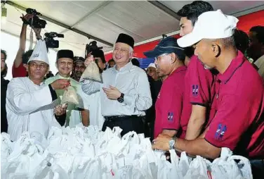  ??  ?? Tasty treats: Najib holding up packets of ‘bubur lambuk’ ready to be given out to the public at the Kampung Baru mosque. Looking on is Nong Chik (second from left). — Bernama